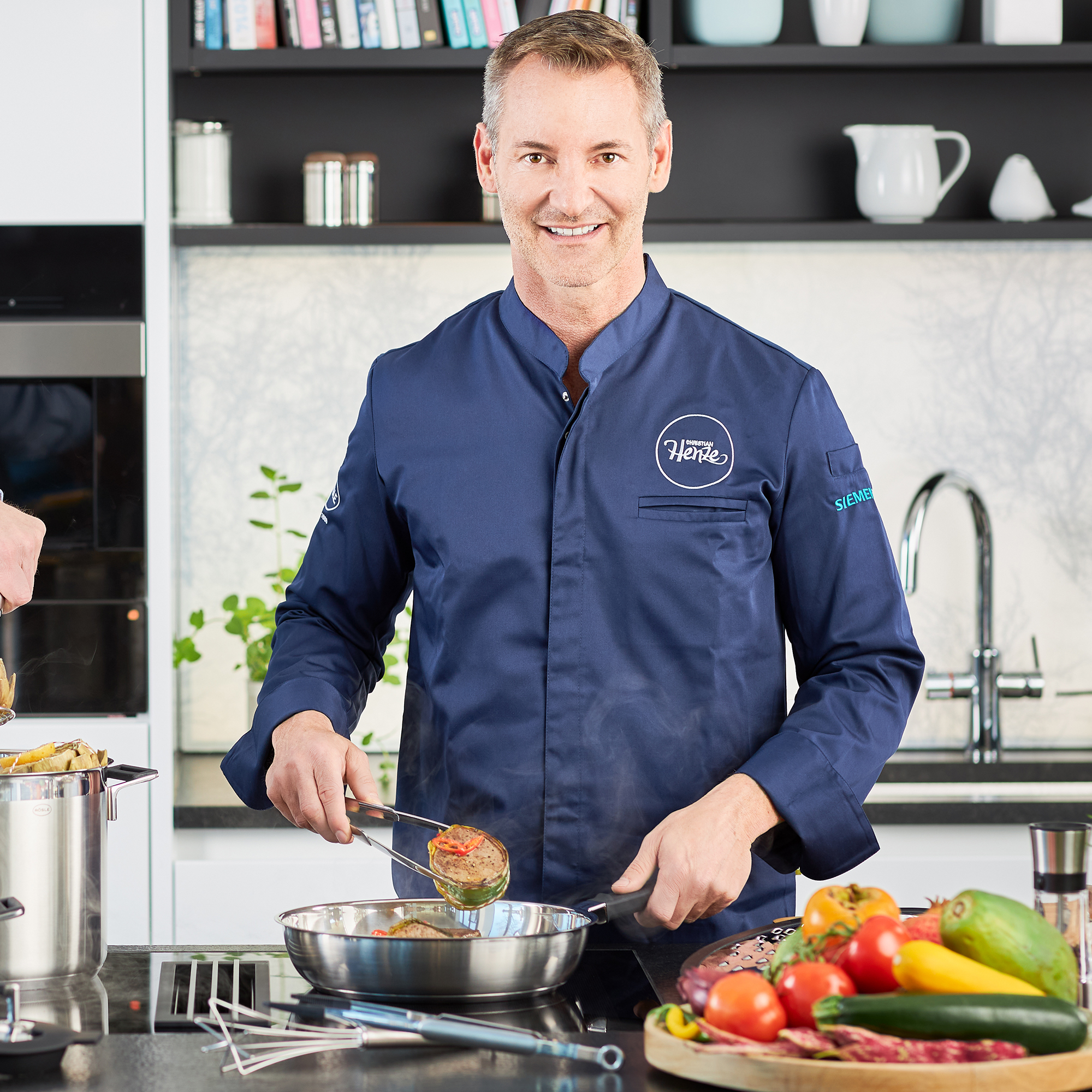 RÖSLE stainless steel frying pan 28 cm in use Stainless steel frying pan, 28 cm, in use by a chef in a blue chef's jacket, smiling, with...