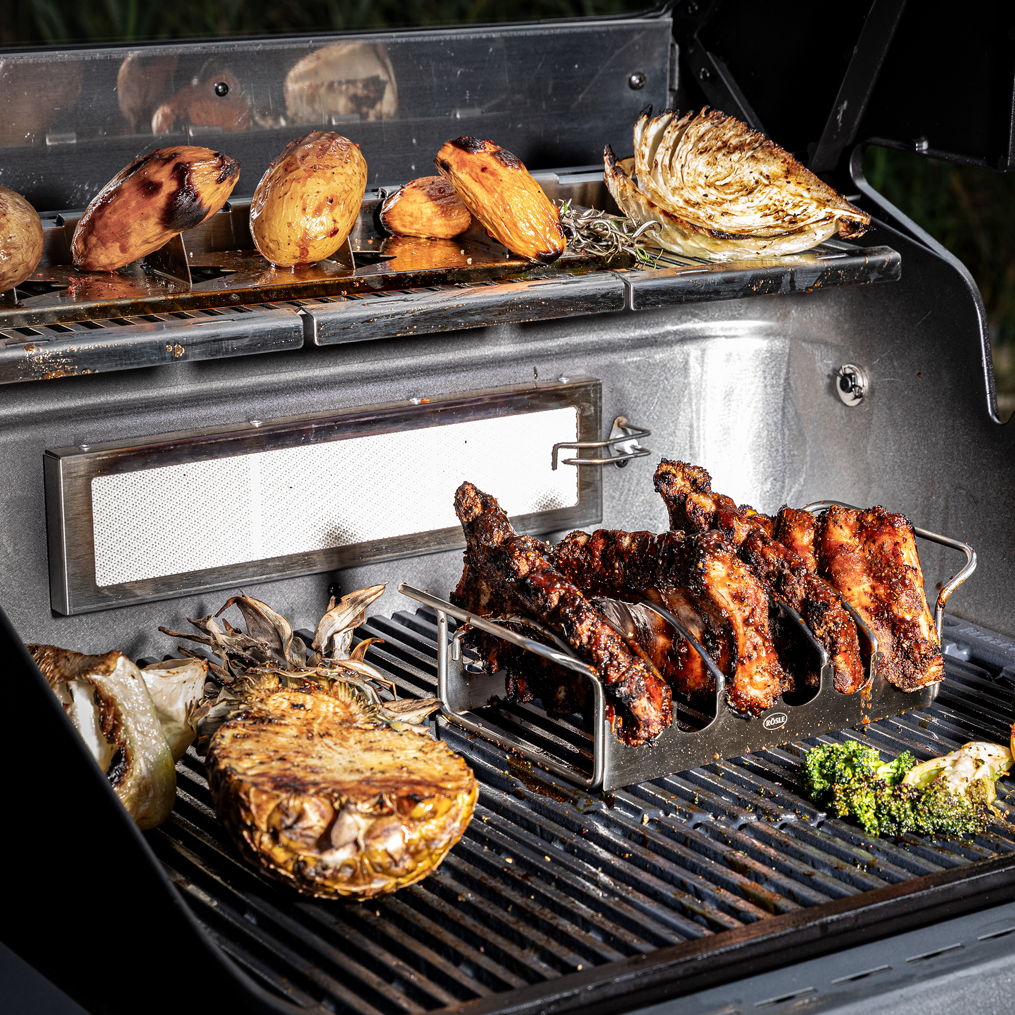 Grill mit gegrilltem Fleisch, Gemüse und Kartoffeln auf dem Rost.