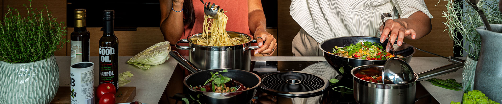 Cooking together with RÖSLE cookware Two people cook together with cookware, one person lifts spaghetti out of a pot, the other...