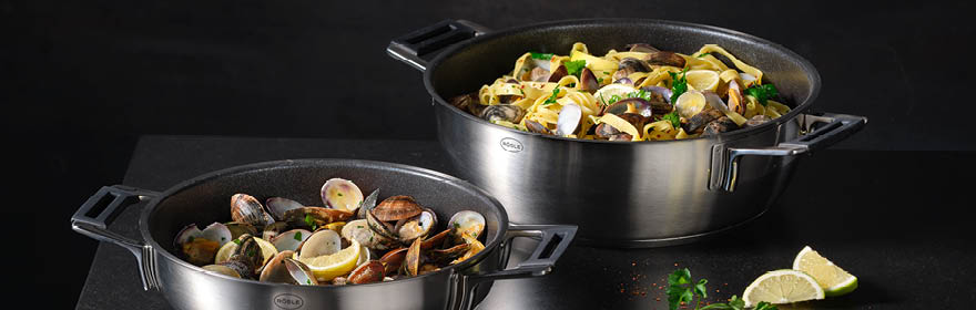 RÖSLE serveerschalen met mosselen en pasta Roestvrijstalen serveerpannen met schelpen en pasta, op een zwarte achtergrond.