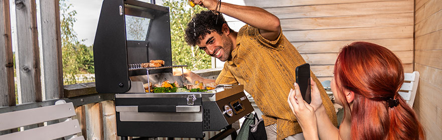 Portable grill Woman photographs man with mobile phone in front of barbecue