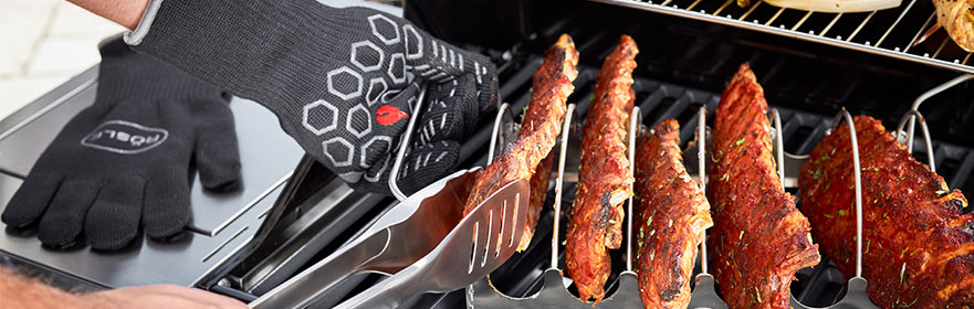 Barbecuehandschoenen en -tangen van RÖSLE Barbecuehandschoenen en barbecuetangen in actie terwijl ribbetjes worden klaargemaakt op de...