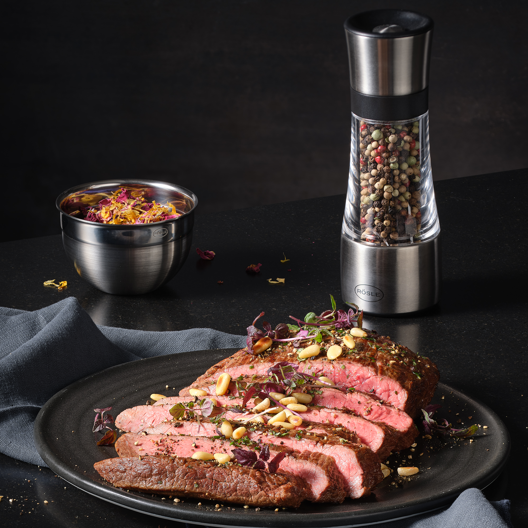 RÖSLE Gewürzmühle und gewürztes Fleisch Gewürzmühle aus Edelstahl neben einem Teller mit in Scheiben geschnittenem, gewürztem Fleisch...