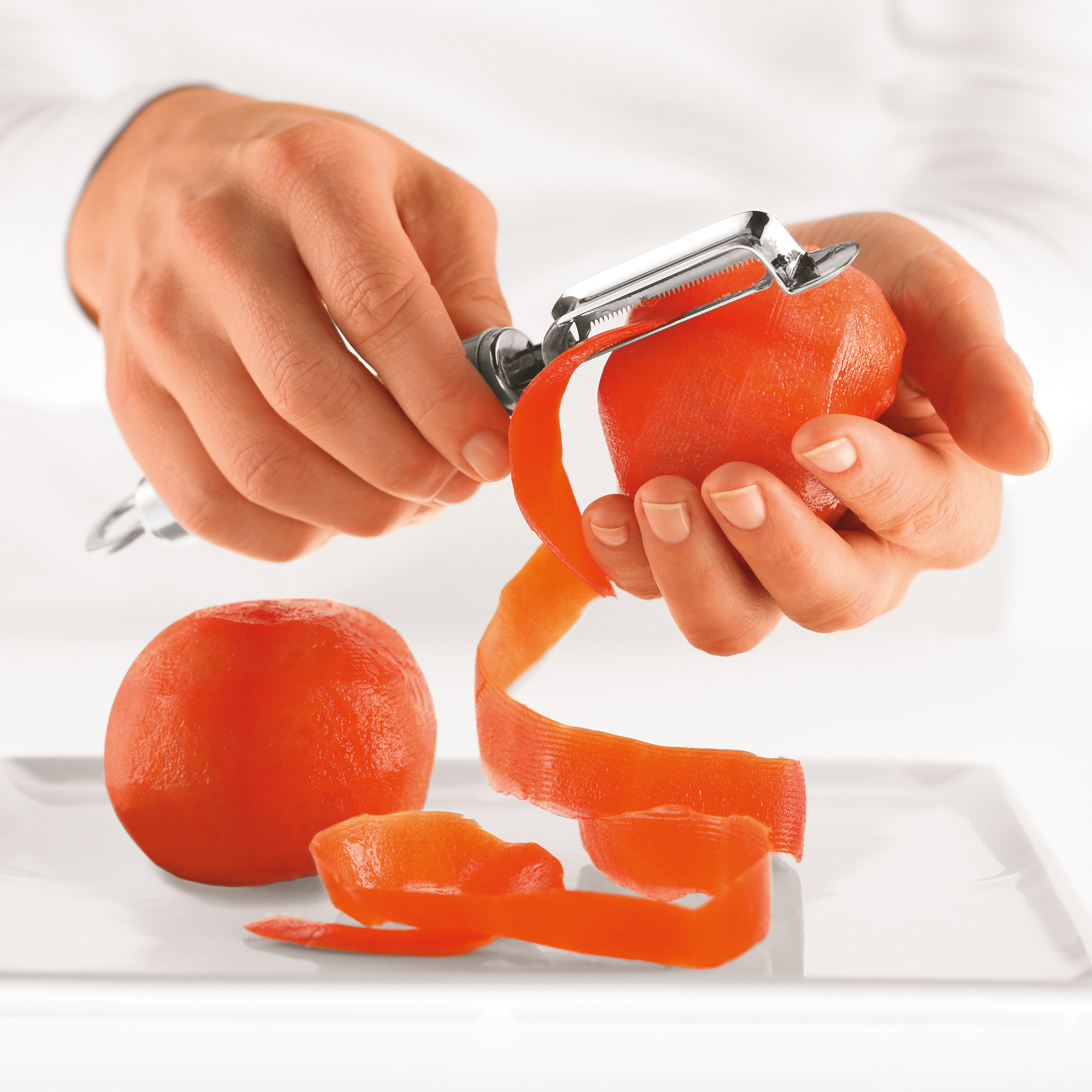 RÖSLE tomato and kiwi peeler Tomato and kiwi peeler in use, one hand peels a tomato, the skin falls off.