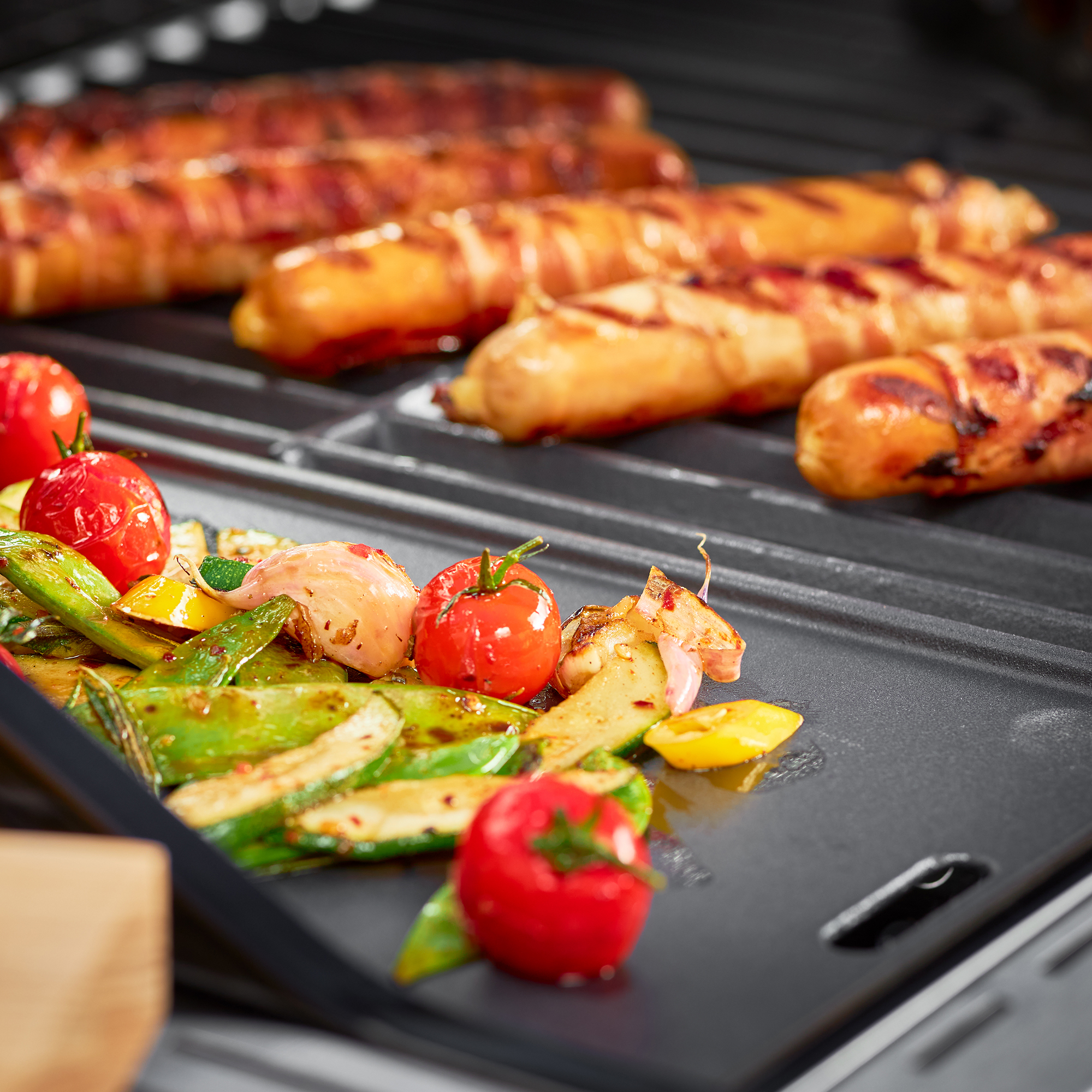 Grillplatte von RÖSLE mit Würstchen und Gemüse Grillplatte mit gegrillten Würstchen und Gemüse, darunter Kirschtomaten und Zuckerschoten.