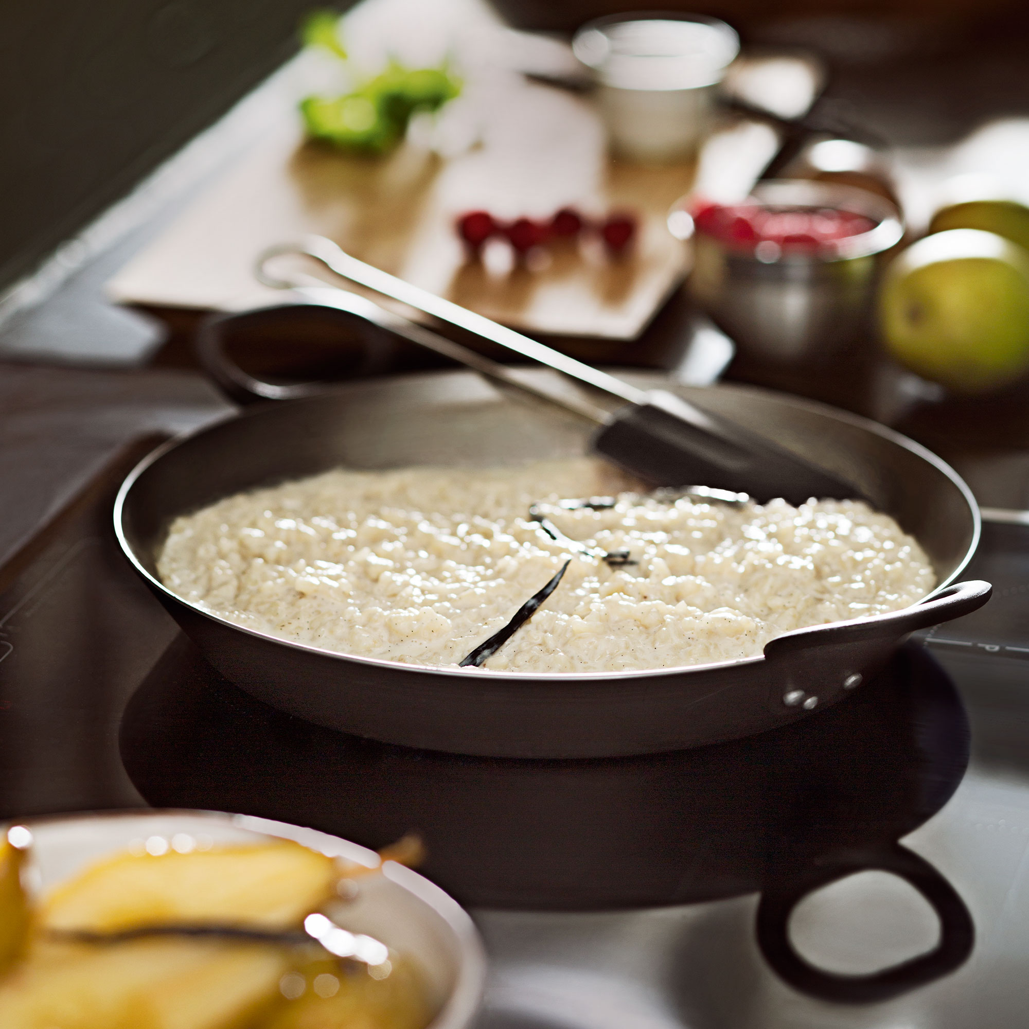 RÖSLE Eisen Servierpfanne mit Risotto Servierpfanne aus Eisen, 24 cm, mit Risotto auf dem Herd, im Hintergrund frische Zutaten.