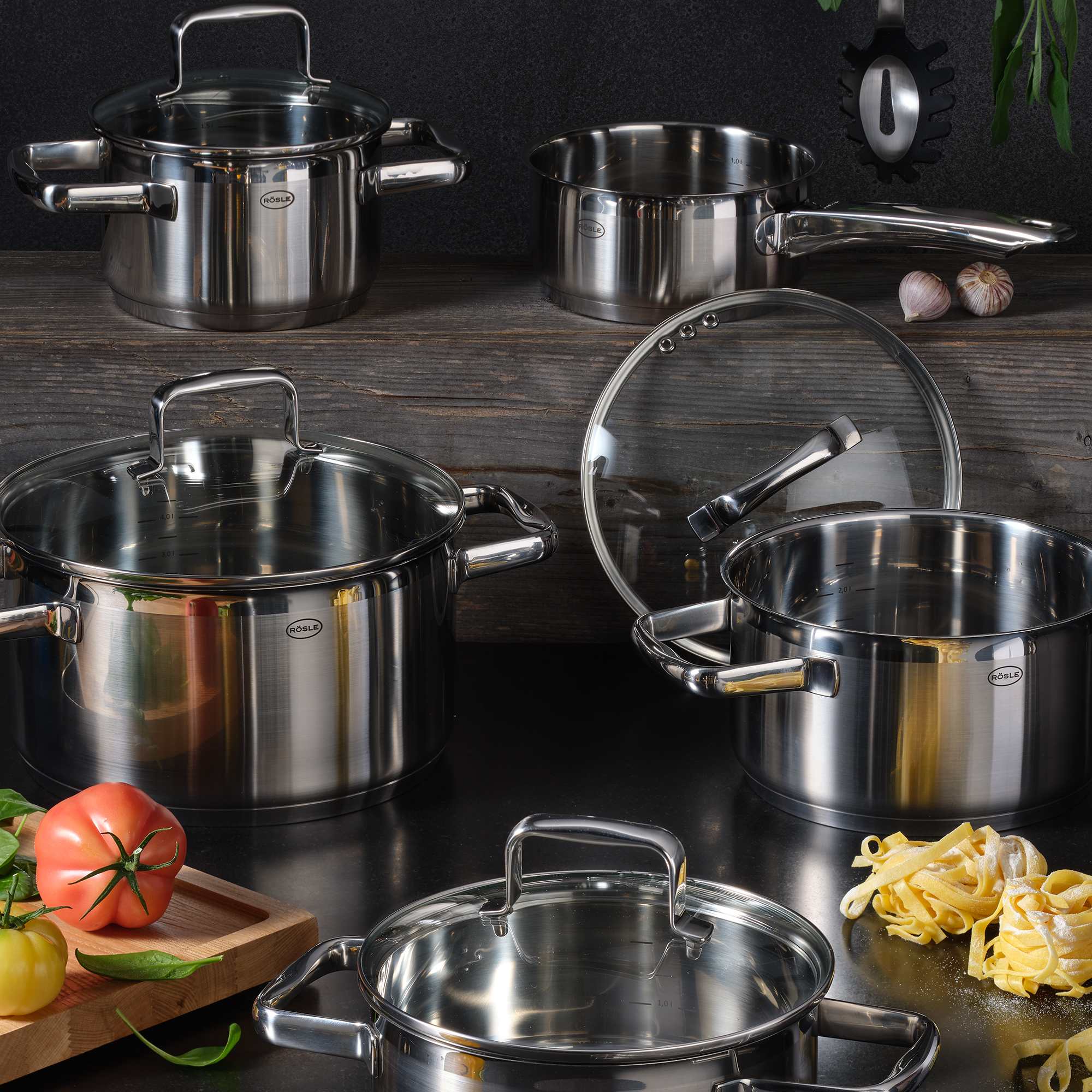 RÖSLE stainless steel roasting pan and cooking pots Stainless steel roasting and cooking pots, various sizes, with glass lids, on a wooden surface.