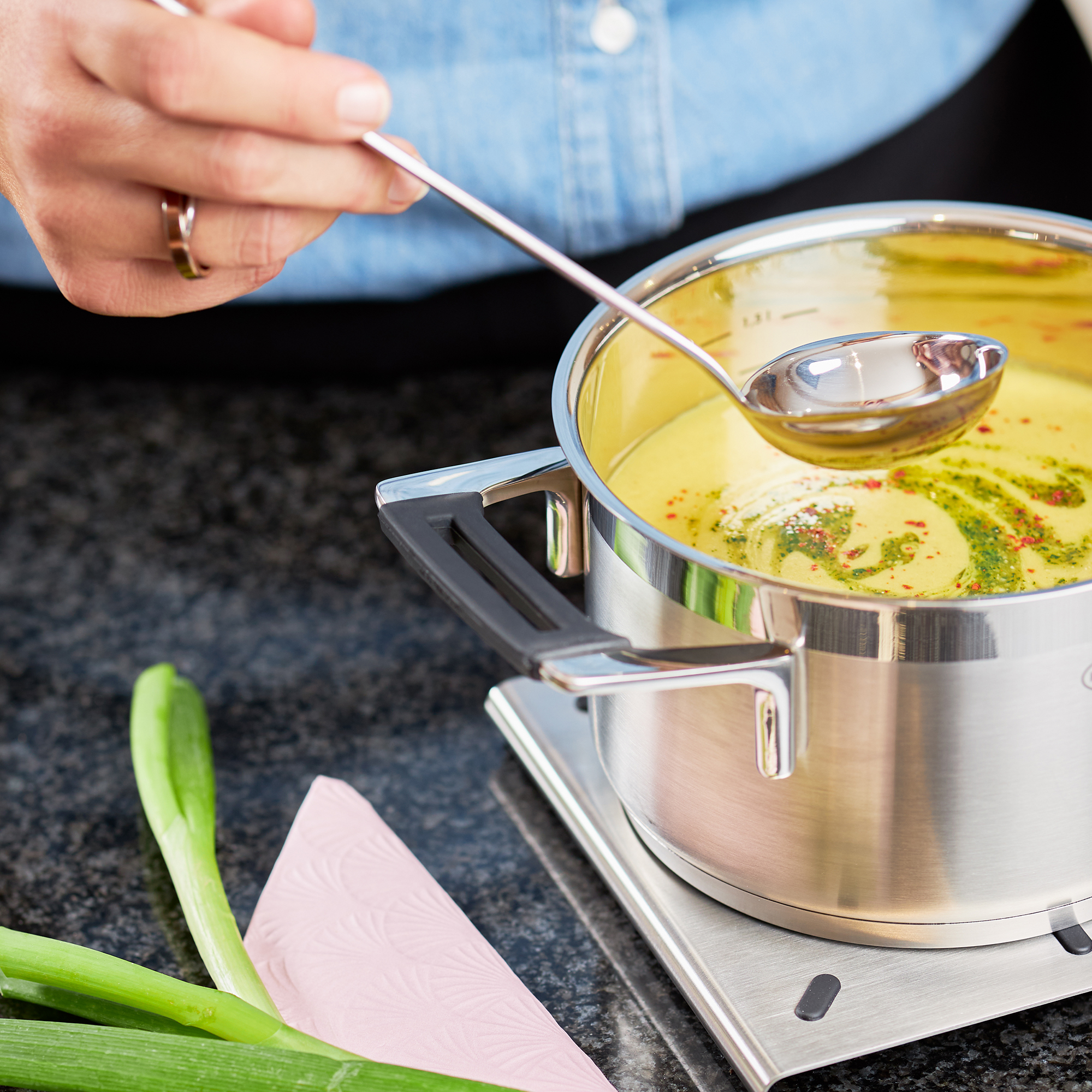 RÖSLE sauce spoon in action Stainless steel sauce spoon, 25 cm, is used to scoop a yellow sauce from a pot.