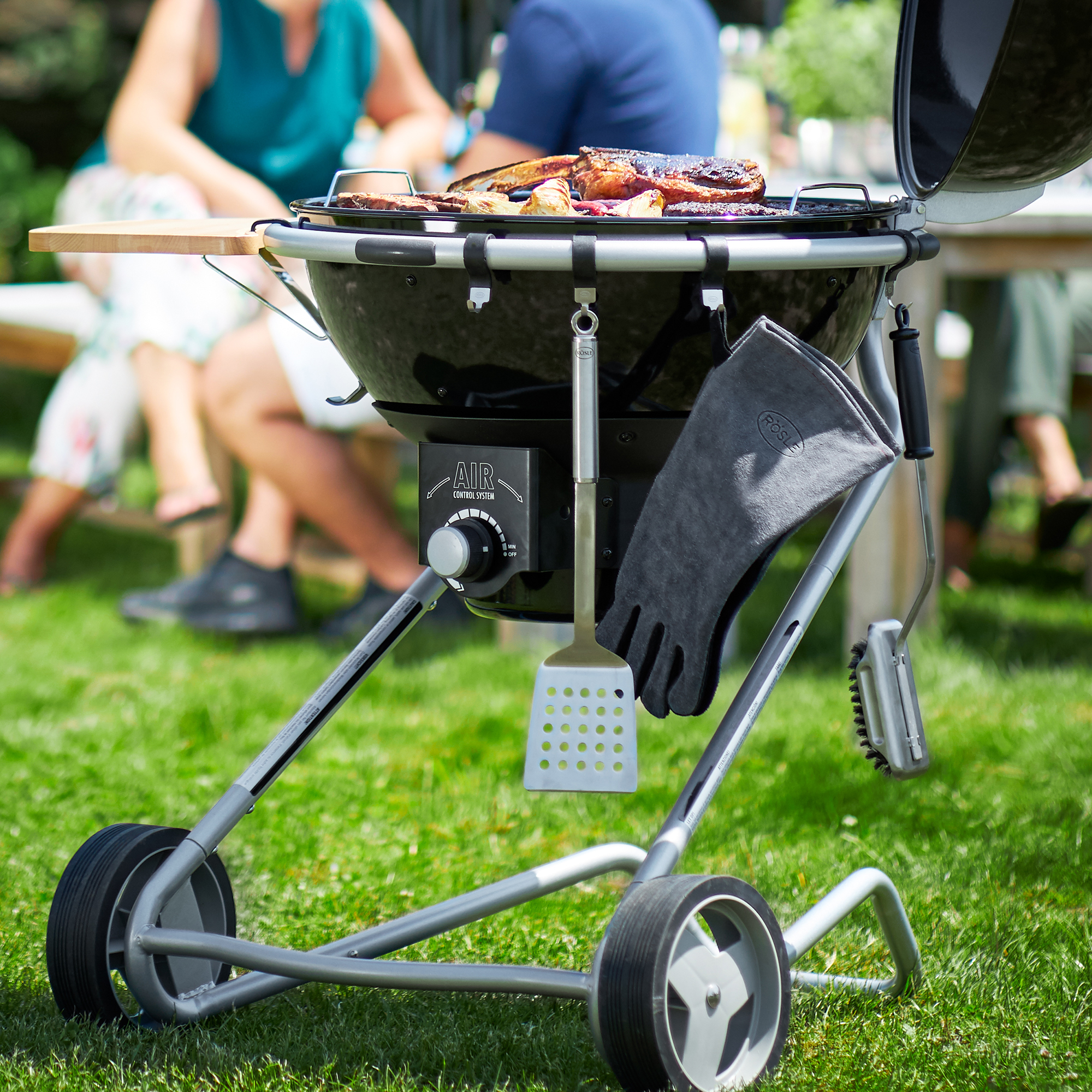 RÖSLE Grill im Garten Grill mit Grillgut auf dem Rost, Grillhandschuh und Grillwerkzeug sichtbar, im Garten auf...