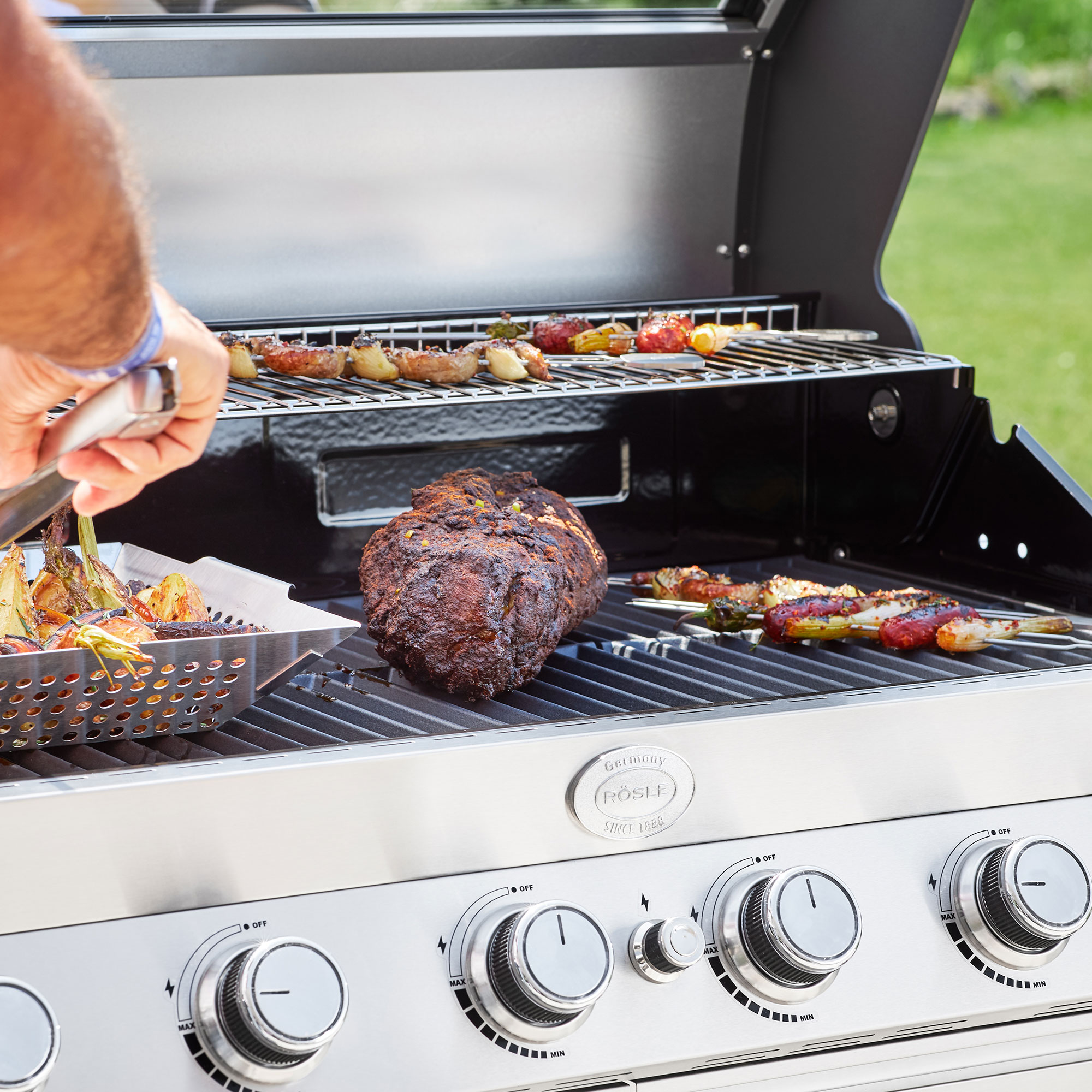 RÖSLE Gasgrill Videro G6-S Gasgrill Videro G6-S aus Edelstahl mit Grillgut auf dem Rost und in einer Grillkorb, im Freien.