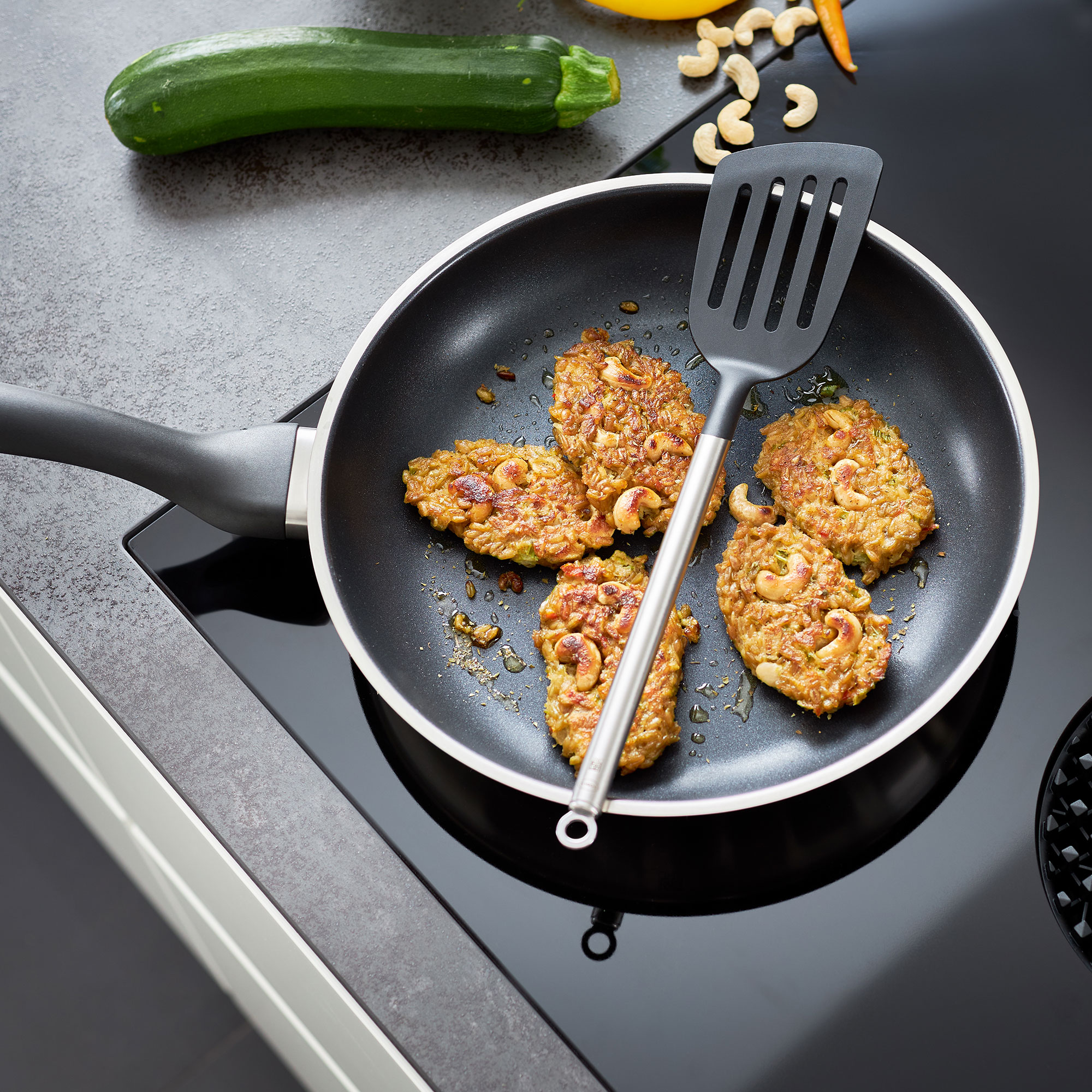 RÖSLE Gourmet-Set mit Pfanne und Spatel Pfanne mit gebratenen Gemüsefrikadellen und einem Spatel auf einem Kochfeld.