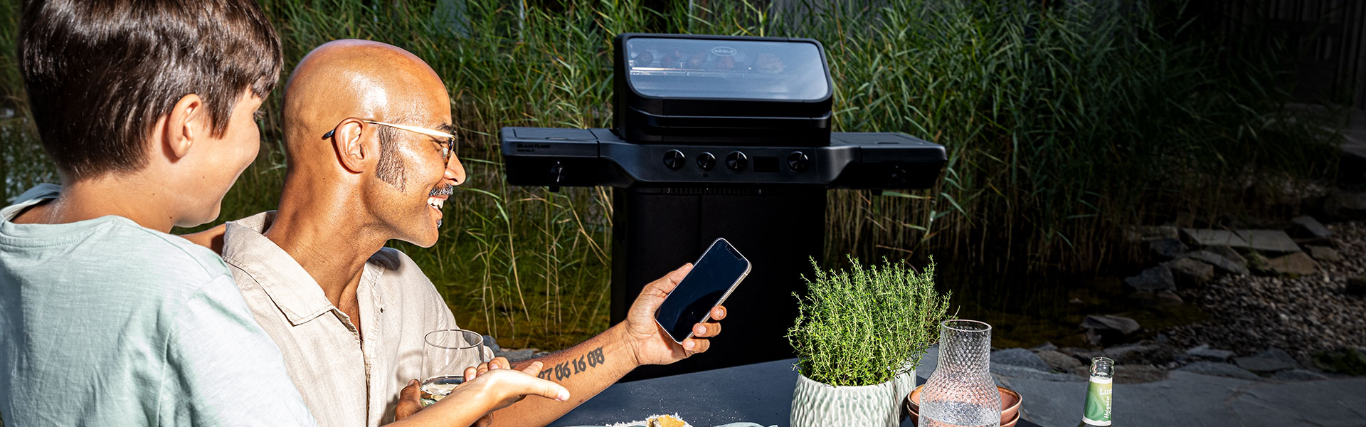 Vater und Sohn stellen gemeinsam die Temperatur des BLAZEFLAME Gasgrills am Handy ein.