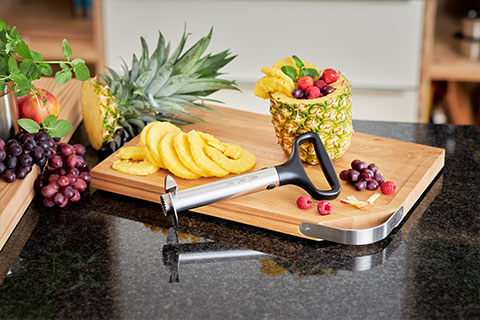 Pineapple Cutter Pro on cutting board with stainless steel handle and cocktail of pineapple next to it.