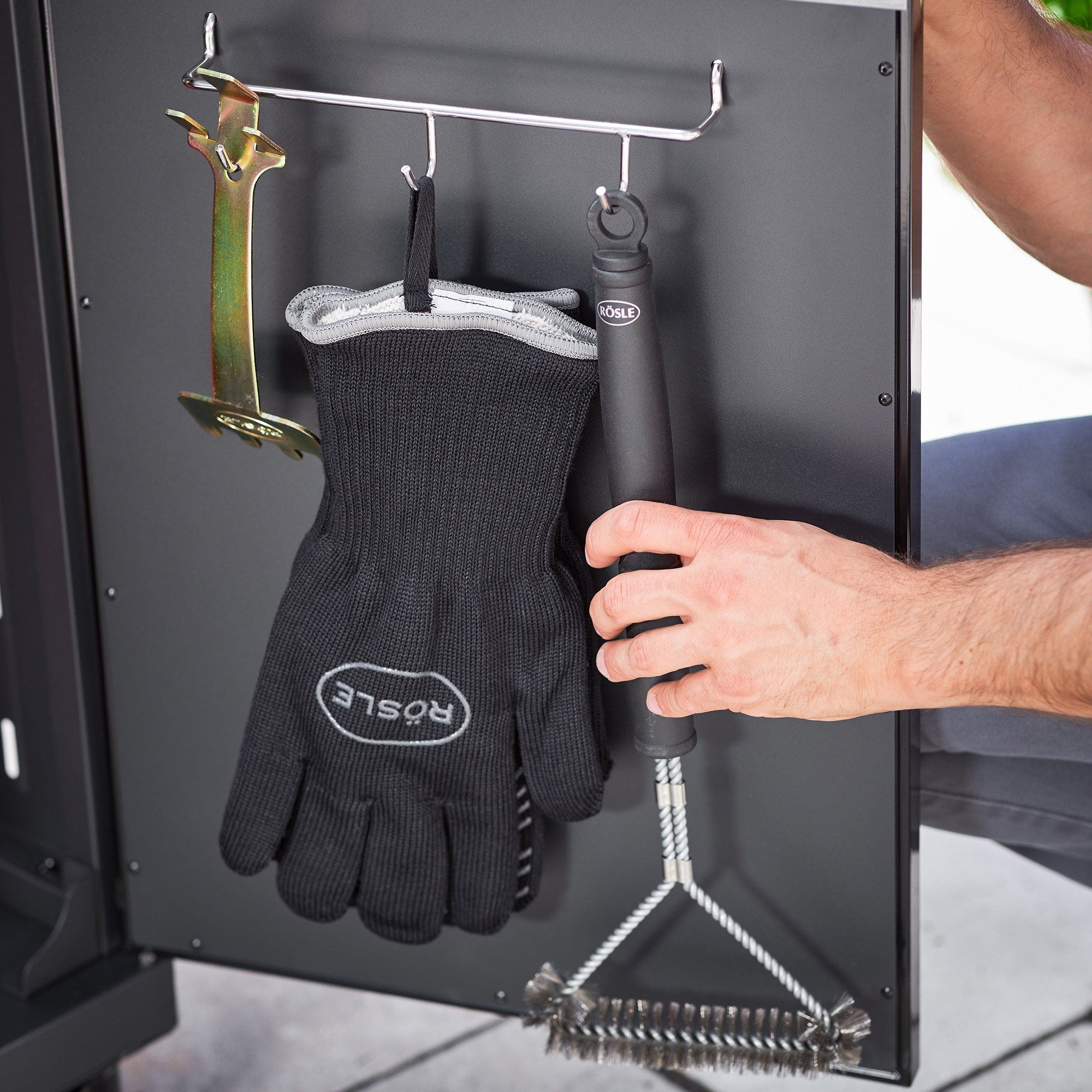 RÖSLE barbecue tools and glove Grill grate cleaning brush, black, with glove and grill tool attached to a holder.
