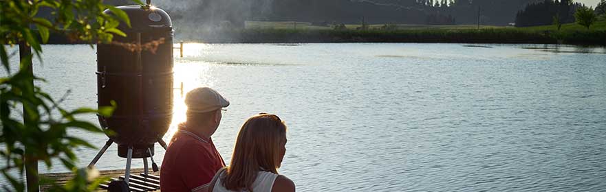 RÖSLE Rookoven aan het water Twee mensen zitten aan het water, een roker op de voorgrond.