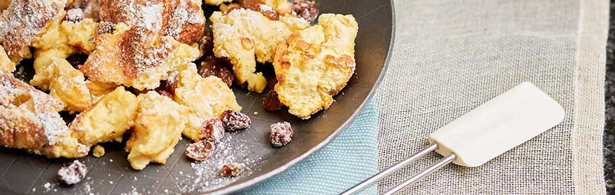 Kaiserschmarrn in RÖSLE Pfanne Pfanne mit Kaiserschmarrn, bestreut mit Puderzucker und Rosinen, auf einem dunklen Teller.