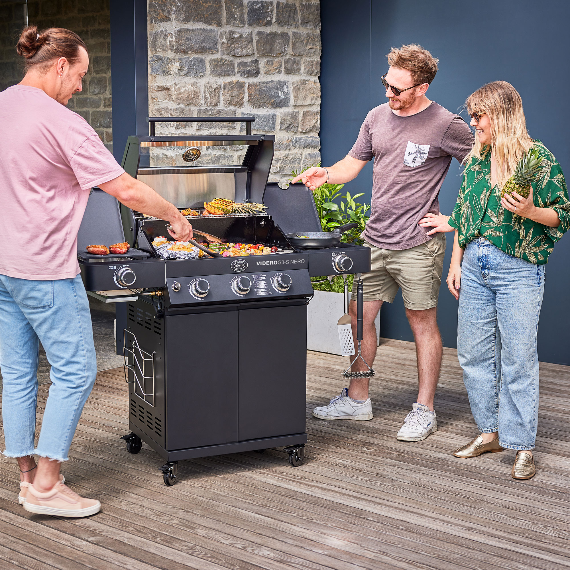 RÖSLE Gasgrill Videro G3-S NERO mit Personen Gasgrill Videro G3-S NERO in Aktion, drei Personen grillen und unterhalten sich.