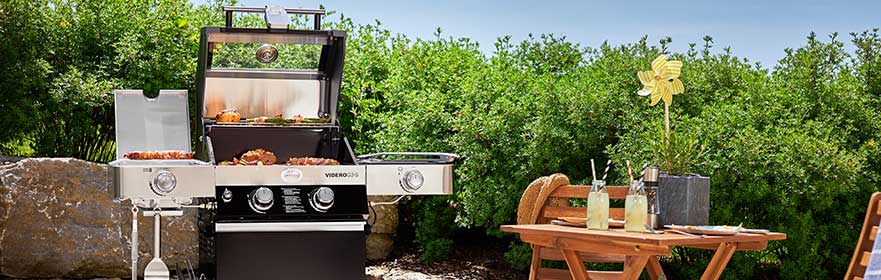 Videro buitenbarbecue op gas, met barbecueoppervlak en zijbrander, omringd door planten en een tafel met drankjes.
