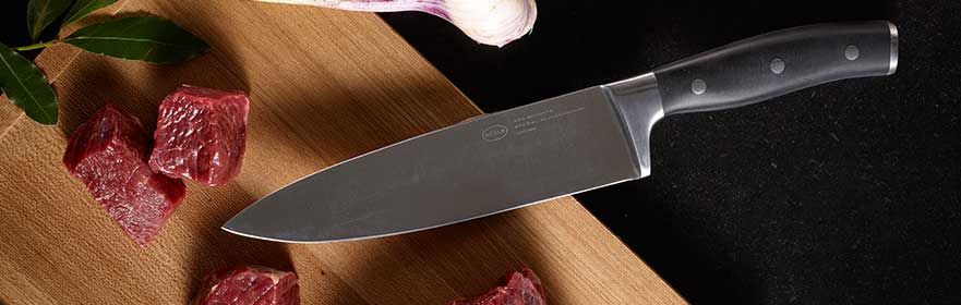 RÖSLE Kochmesser der Serie Tradition Kochmesser der Serie Tradition mit schwarzem Griff und Edelstahlklinge, umgeben von Fleischstücken...