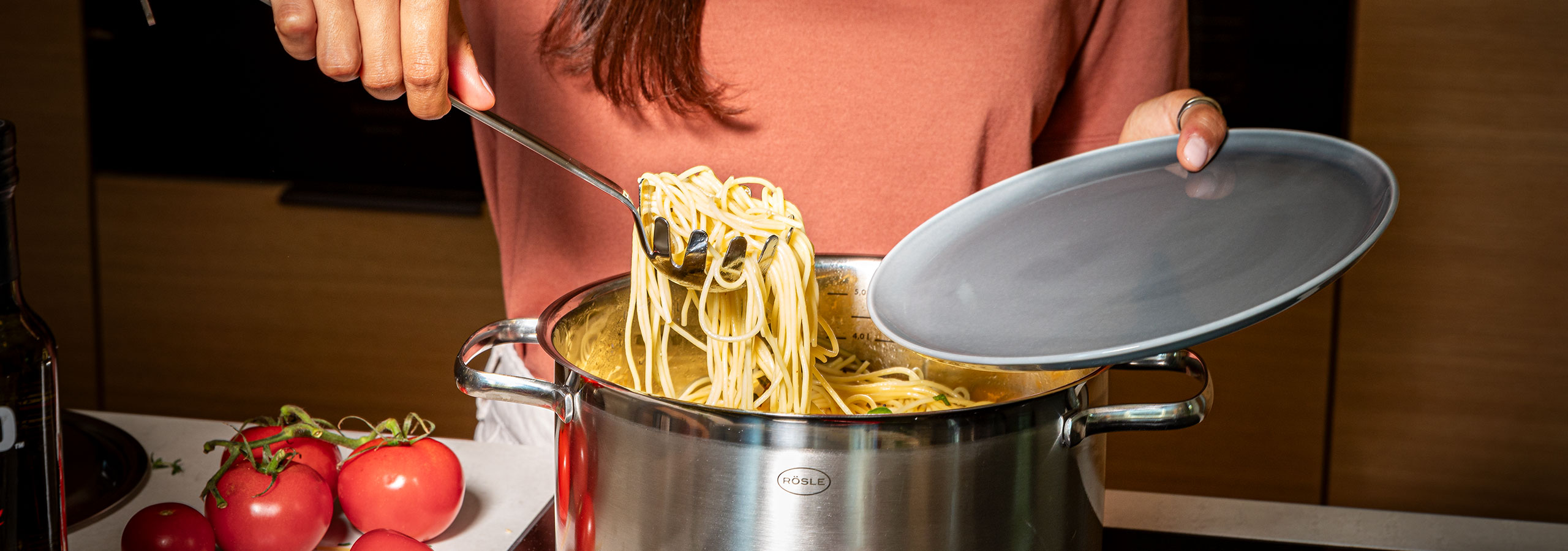 Kitchen gadgets Woman uses the spaghetti lifter to get spaghetti out of the pot onto a plate.