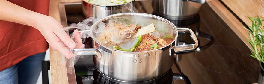 RÖSLE Charm Kochtopf auf Herd Charm Kochtopf aus Edelstahl mit dampfendem Inhalt auf einem Herd, Hand greift den Topf.