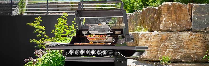 RÖSLE Magnum Grill im Freien Magnum Grill mit geöffnetem Deckel, Grillfläche mit Gemüse und Fleisch, umgeben von Pflanzen...