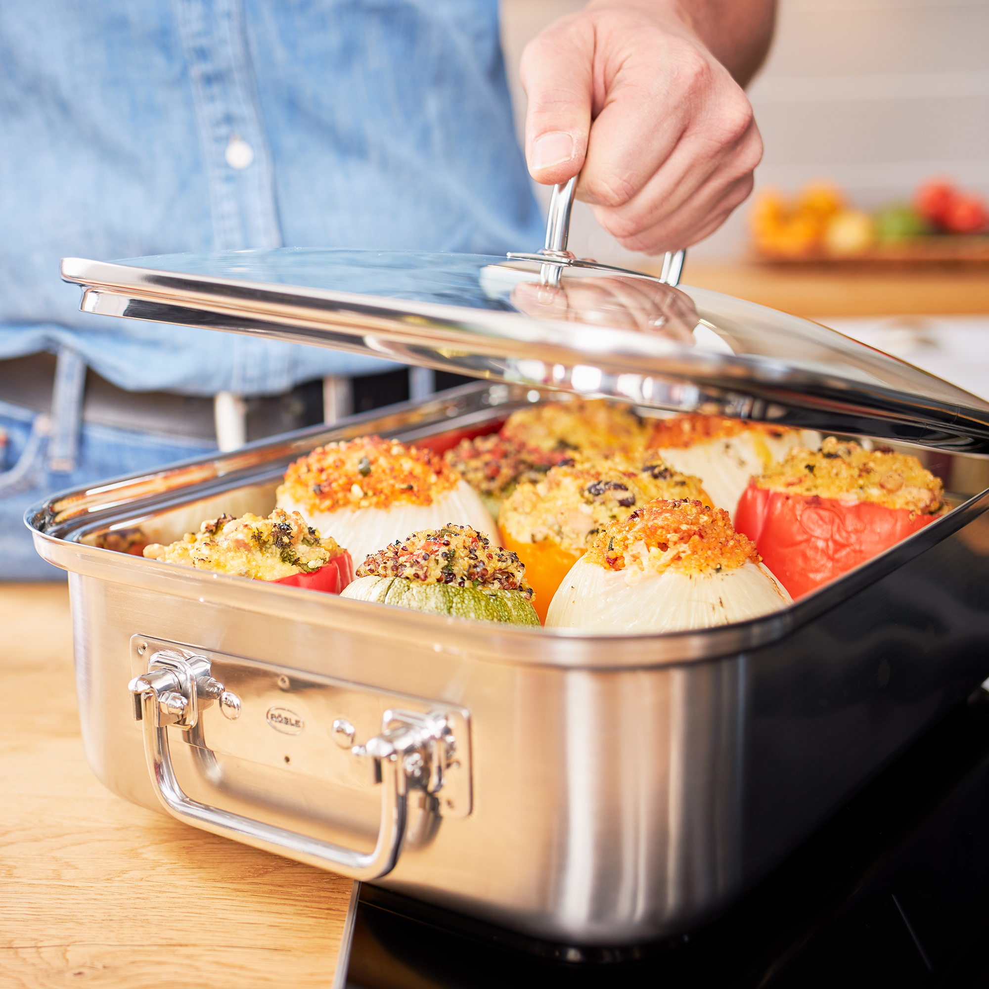 RÖSLE rechteckiger Bräter mit gefülltem Gemüse rechteckiger Bräter aus Edelstahl mit gefüllten Paprika und Zucchini, Deckel wird angehoben.
