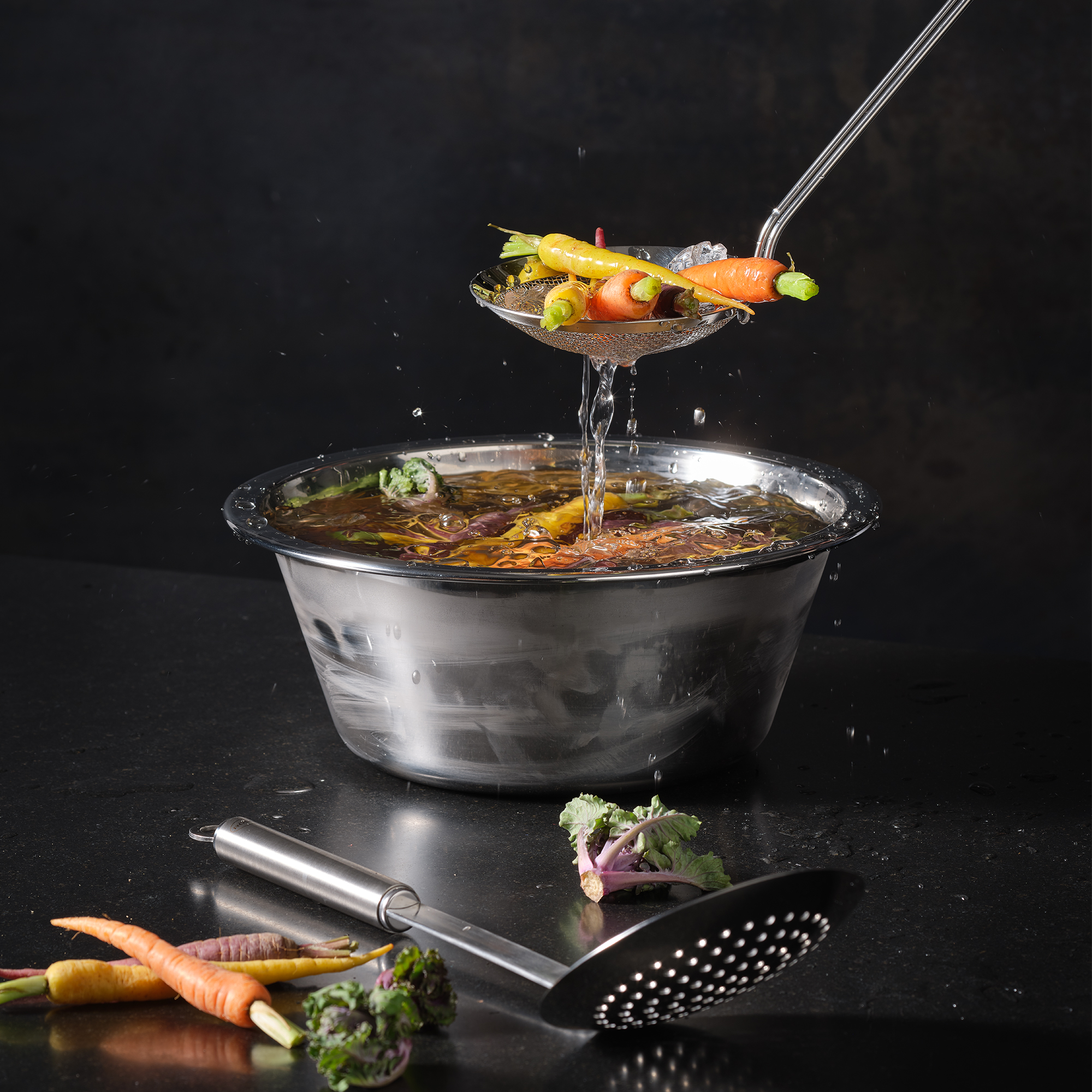 RÖSLE konische Schüssel mit Gemüse konische Schüssel aus Edelstahl mit Gemüse und einem Sieblöffel, der Gemüse heraushebt.