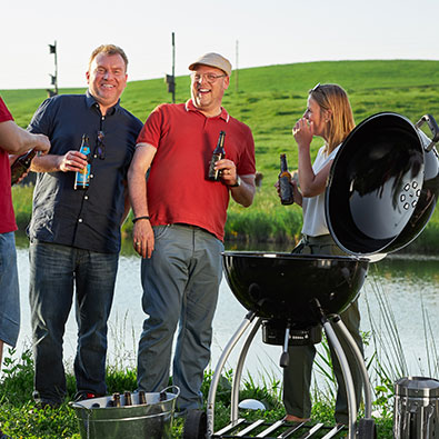 Three friends stand around barbecue by the lake and barbecue together.