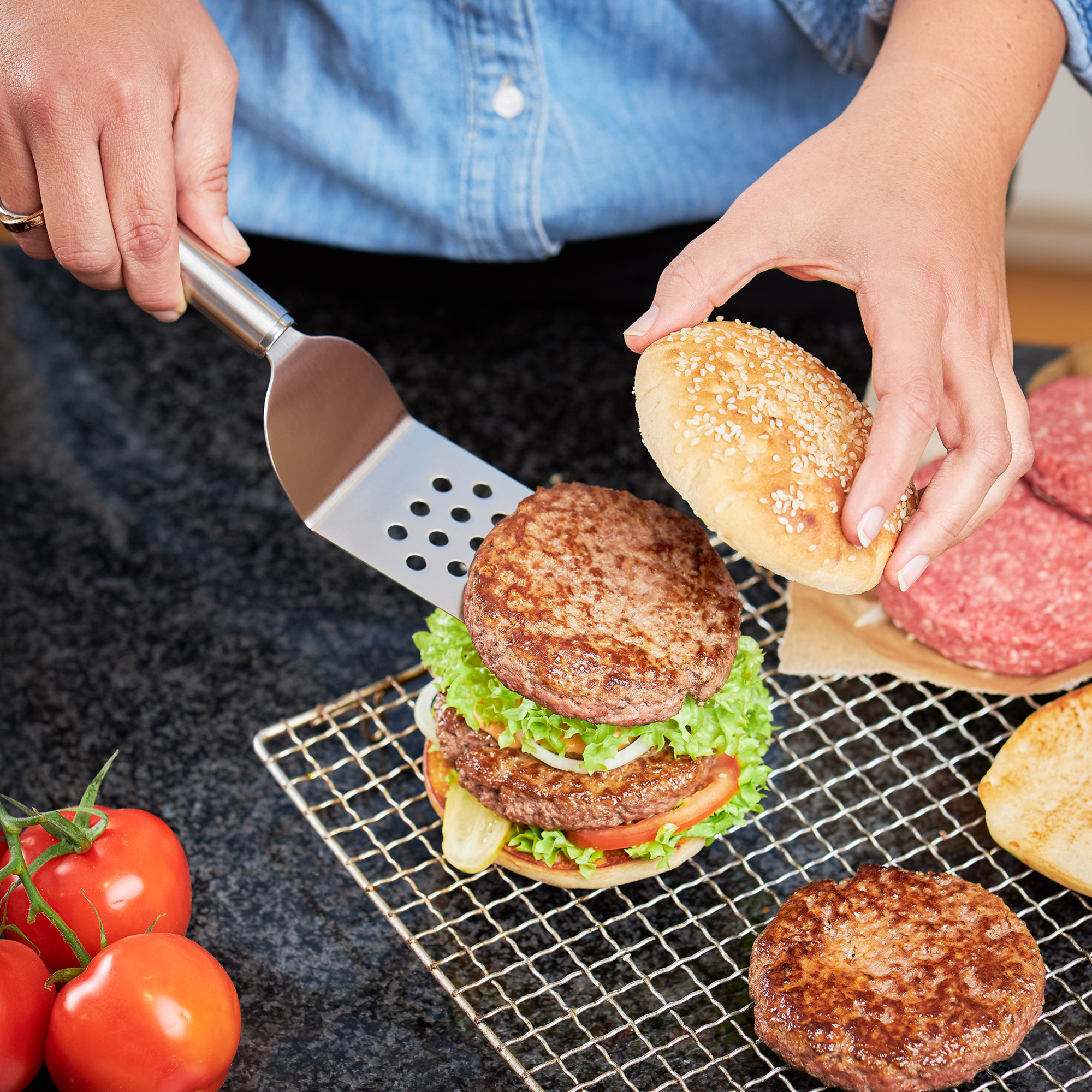 RÖSLE sandwich pallet in action building burgers Sandwich pallet lifts a burger with lettuce, tomatoes and onions, while a bun is placed on...