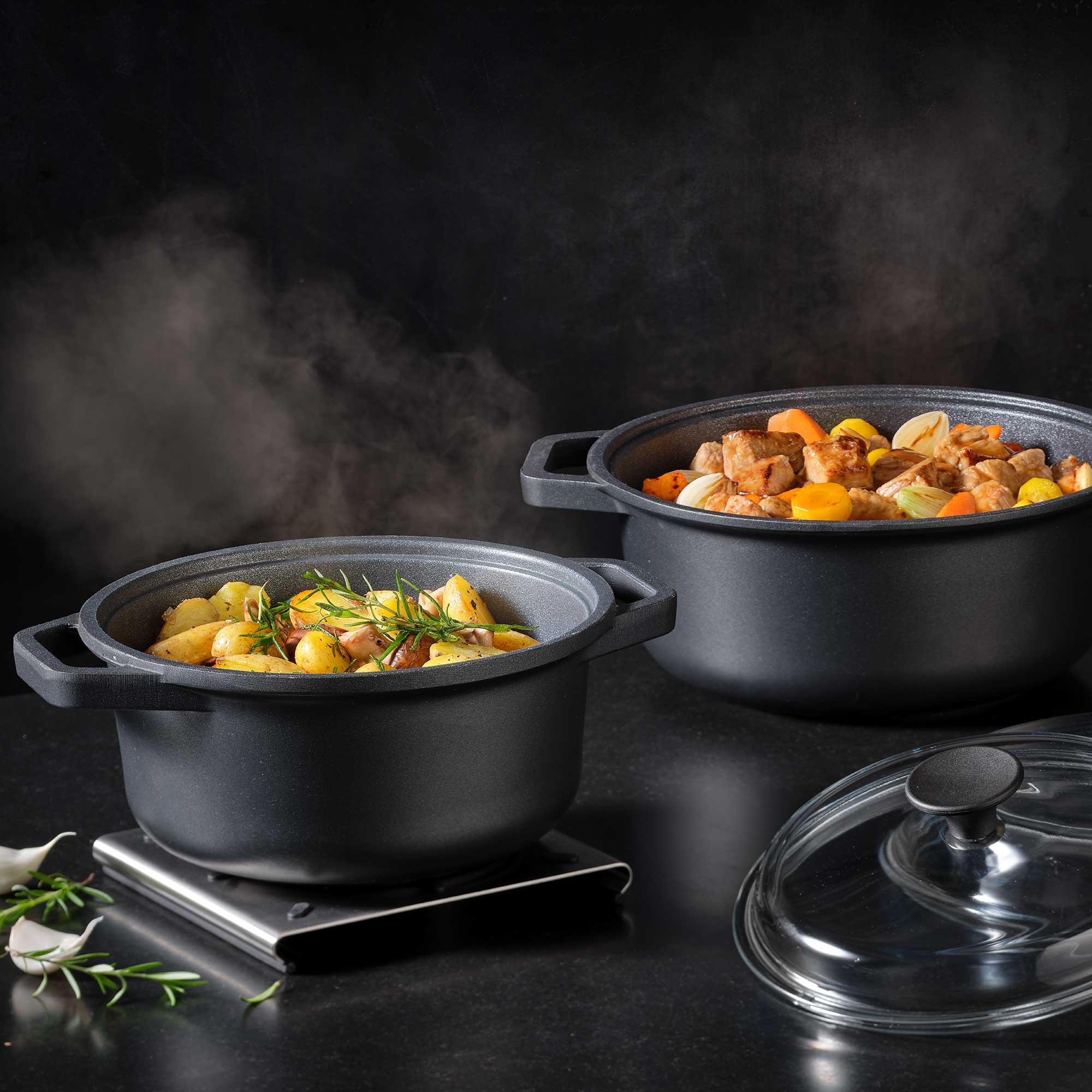 RÖSLE Kochtöpfe Cadini 20cm Kochtöpfe Cadini in Schwarz, einer mit Deckel, gefüllt mit Gemüse und Fleisch, dampfend.