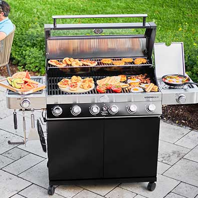 Gas grill with open lid and diveres food on grill grate.