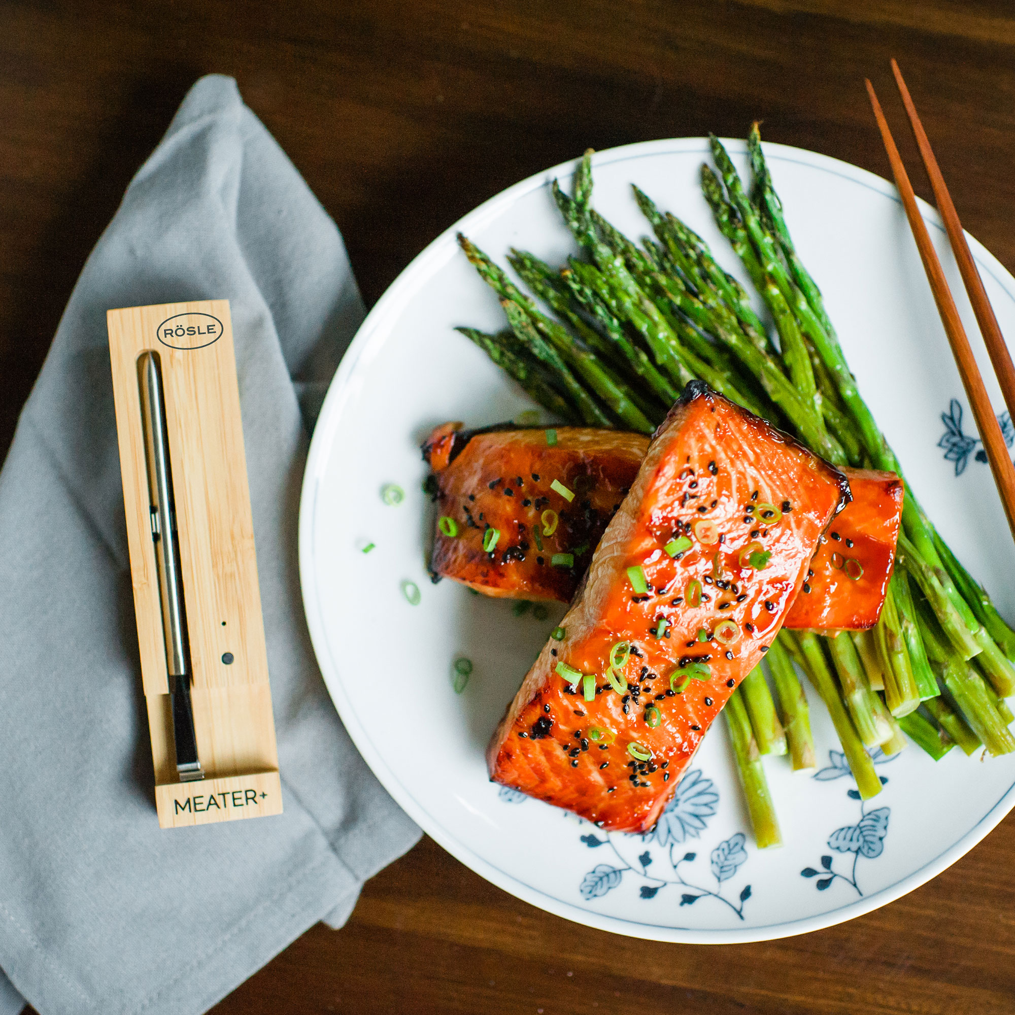 RÖSLE MEATER+ Thermometer und gegrilltes Essen MEATER+ Thermometer neben gegrilltem Lachs und Spargel auf einem Teller.