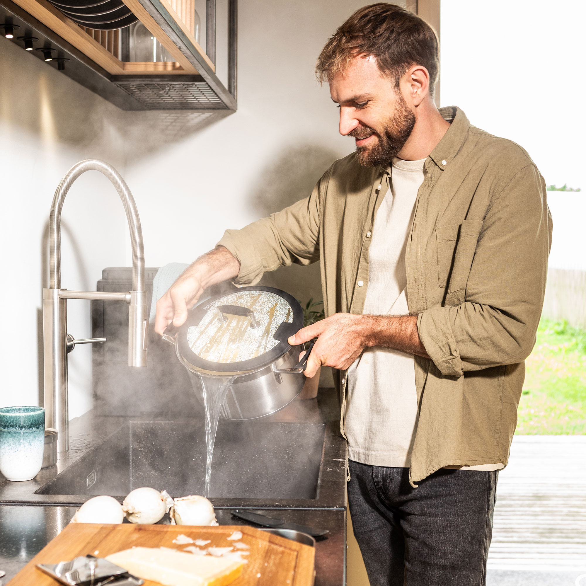 Man in the kitchen with a pot Man in a modern kitchen pouring water from a pot into the sink while standing at a hob.