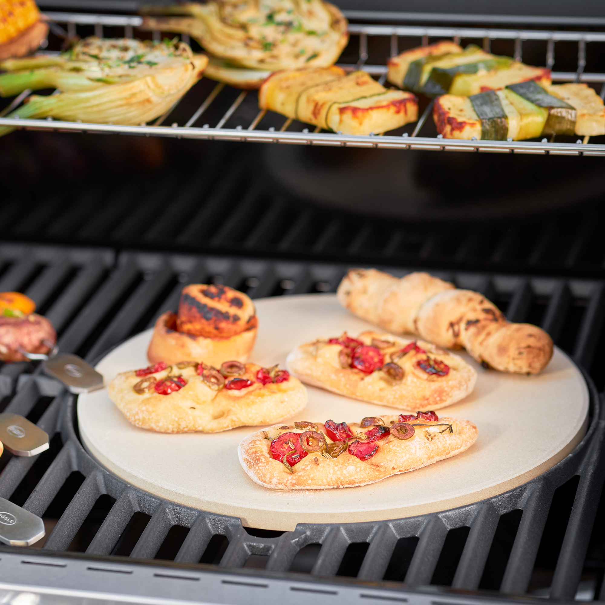 RÖSLE Pizzastein Vario mit belegten Fladenbroten Pizzastein Vario, 30 cm, mit belegten Fladenbroten und Gemüse auf einem Grillrost.