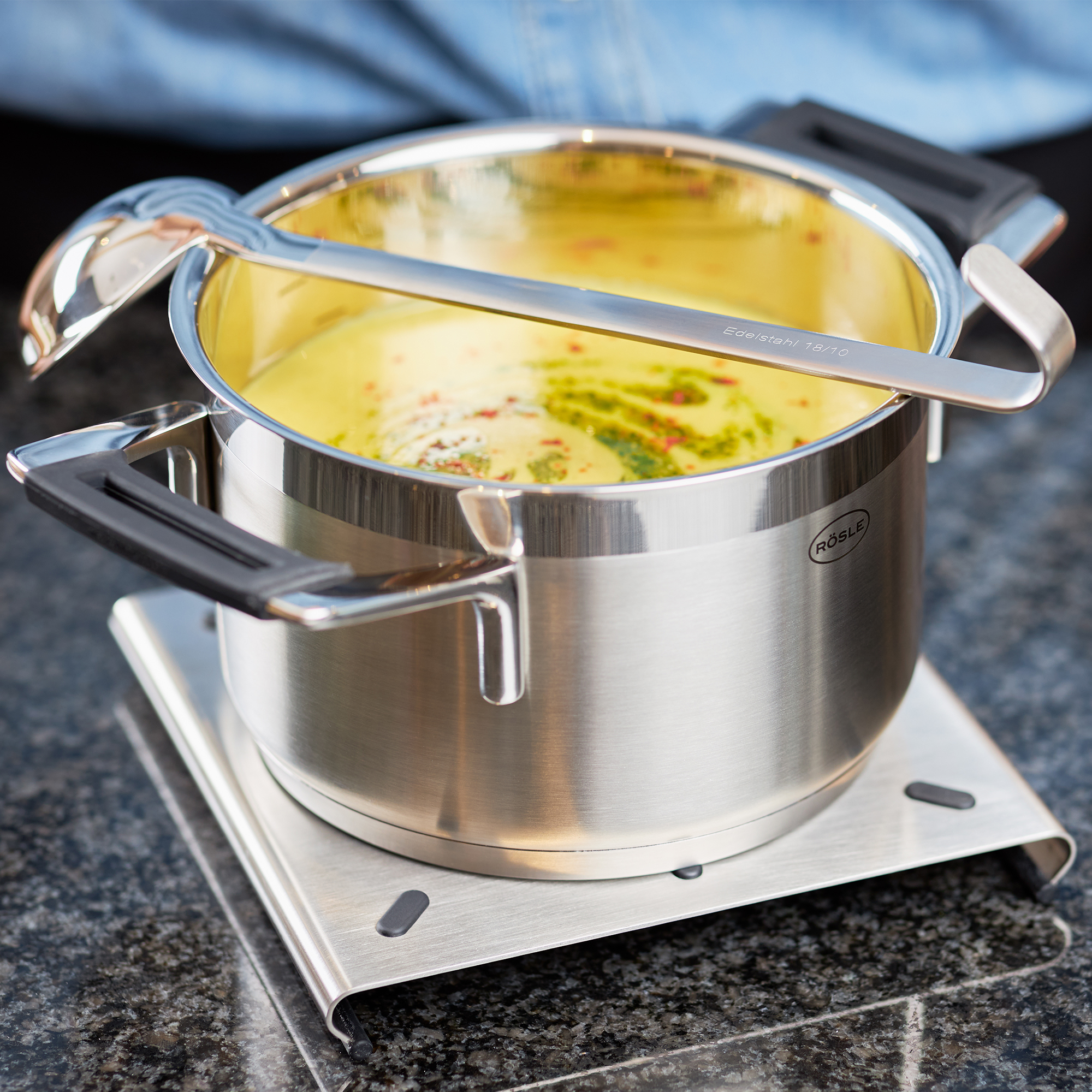 RÖSLE sauce spoon over a pot Stainless steel sauce spoon, 25 cm long, placed over a pot of yellow sauce.