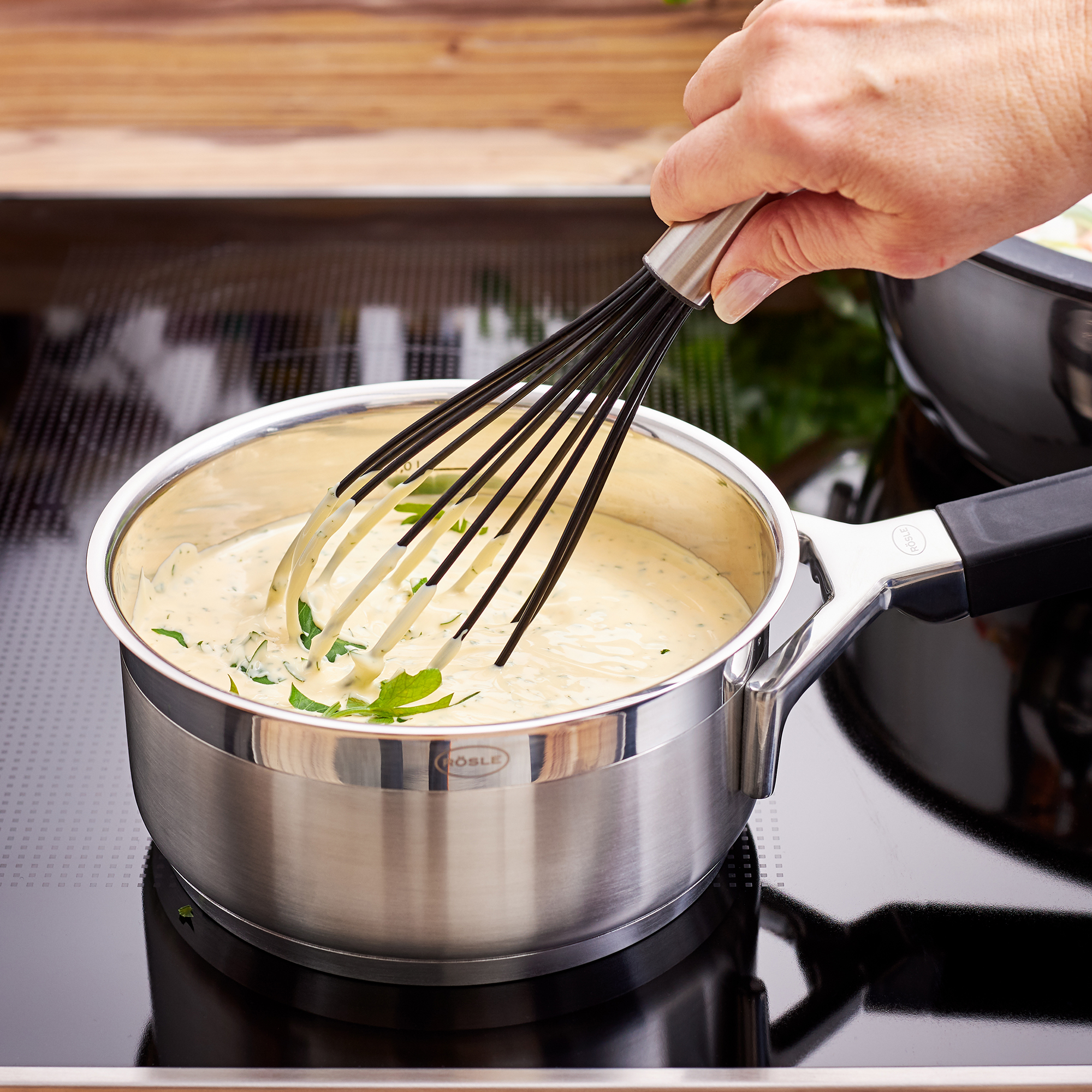 RÖSLE silicone whisk in action Silicone whisk, 27 cm, in a stainless steel pan with a creamy sauce and fresh herbs.