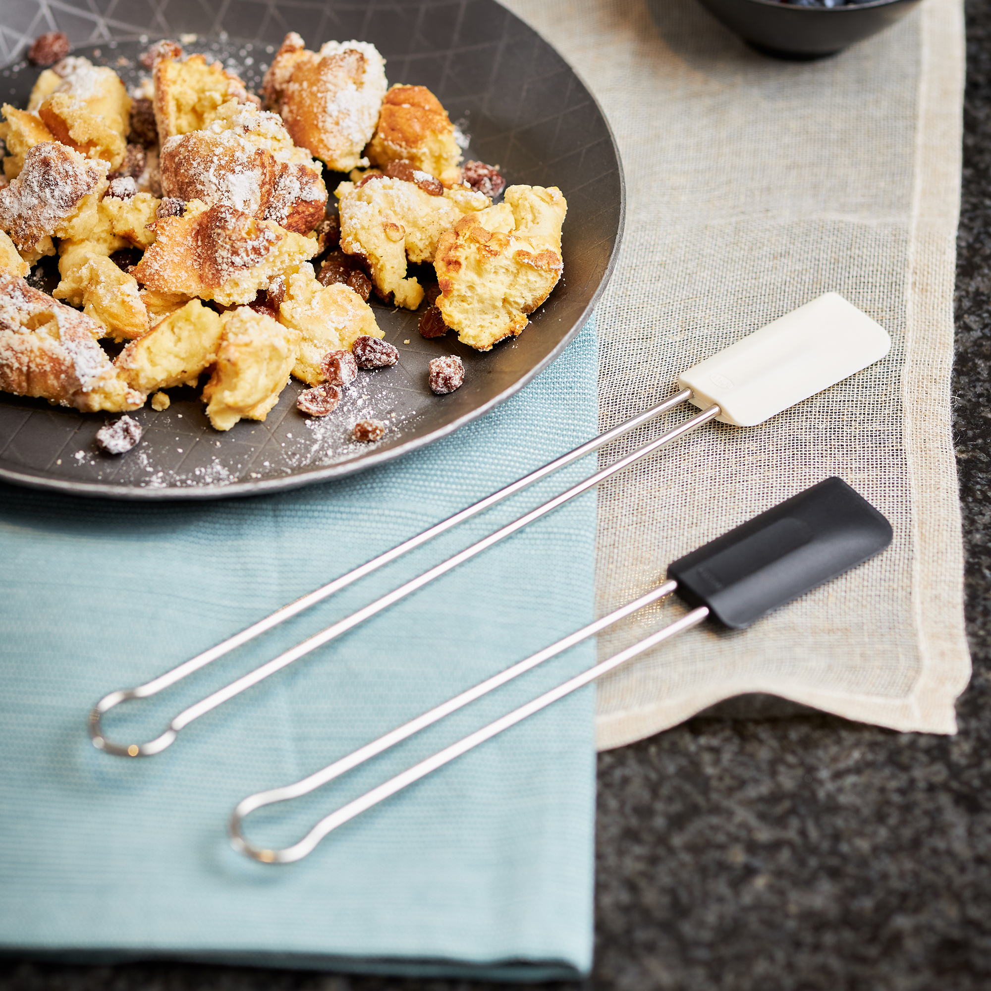 RÖSLE Teigschaber schwarz und weiß Teigschaber in Schwarz und Weiß, aus Edelstahl, neben einem Teller mit süßem Gebäck.