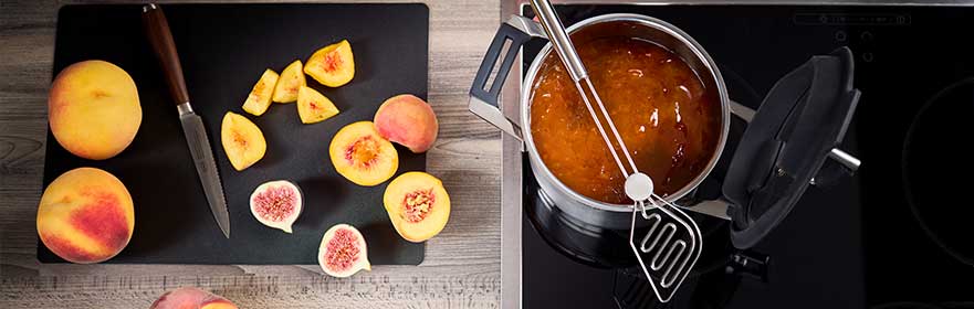 Peaches and figs on the cutting rest next to the Silence Pro saucepan 20 cm with jam