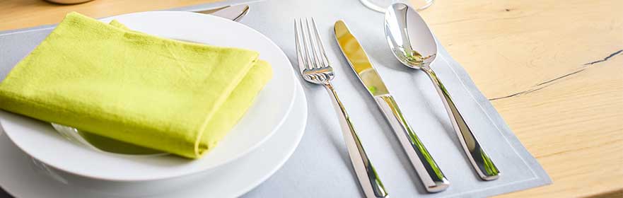 RÖSLE bestekset op gedekte tafel Bestek gedekt op een tafel met een wit bord en groene servetten.