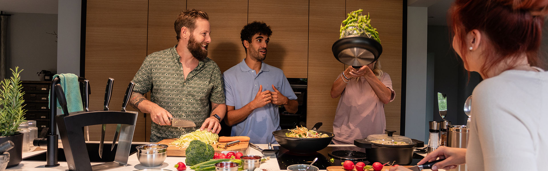 Gemeinsames Kochen in der modernen Küche Gruppe von vier Personen in einer modernen Küche, die gemeinsam kochen und Gemüse zubereiten.