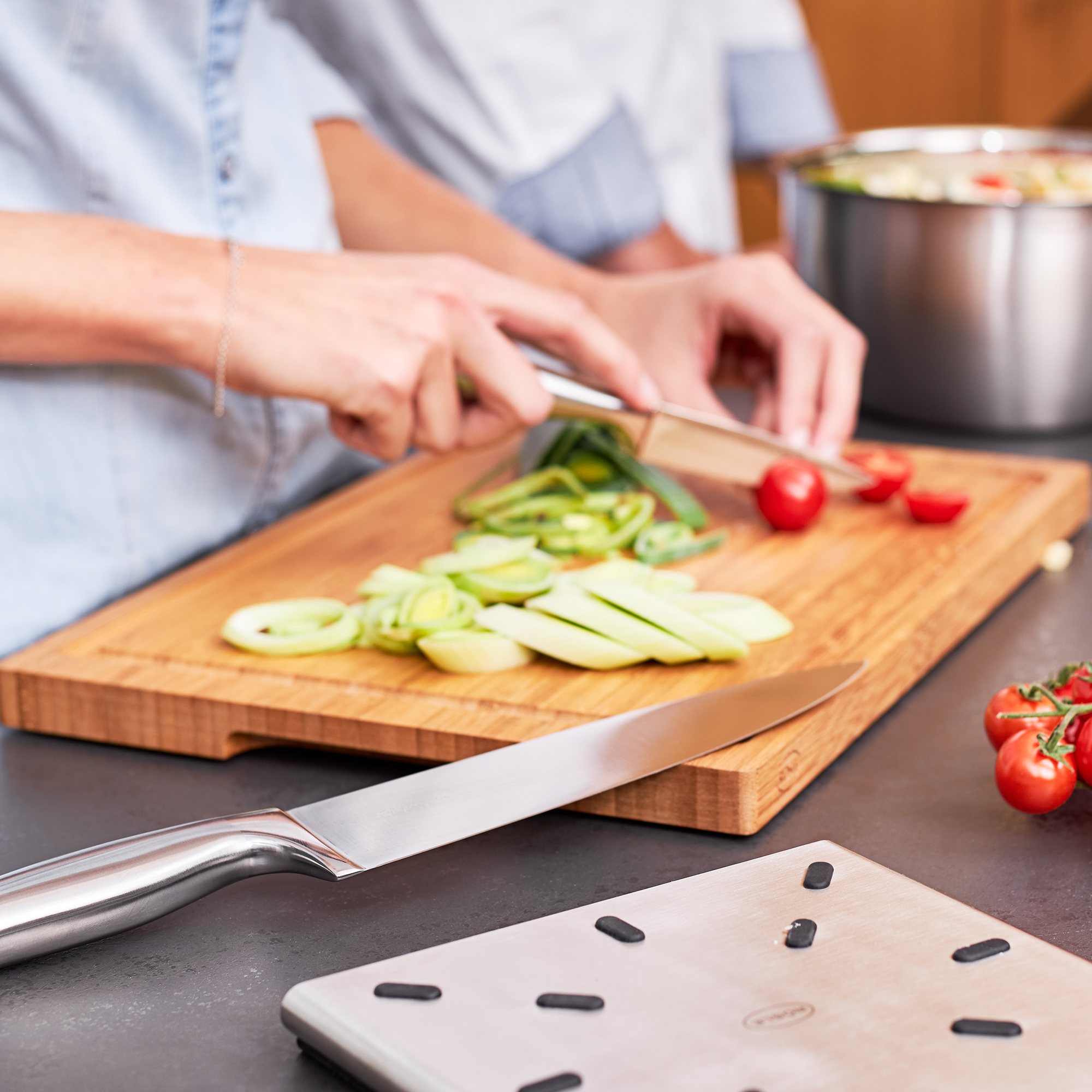 RÖSLE Holzschneidbrett in Aktion Schneidbrett aus Holz in der Nutzung, mit frischem Gemüse und einem Kochmesser.