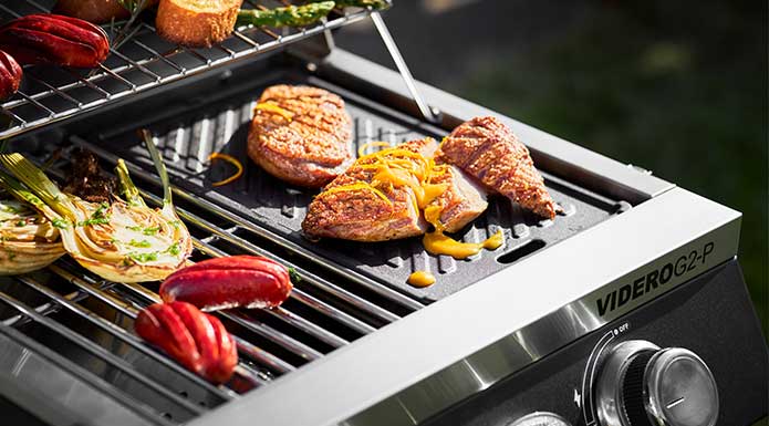 RÖSLE Gasgrill BBQ-Portable Videro G2-P Grillplatte mit Fleisch auf dem Videro G2-P.