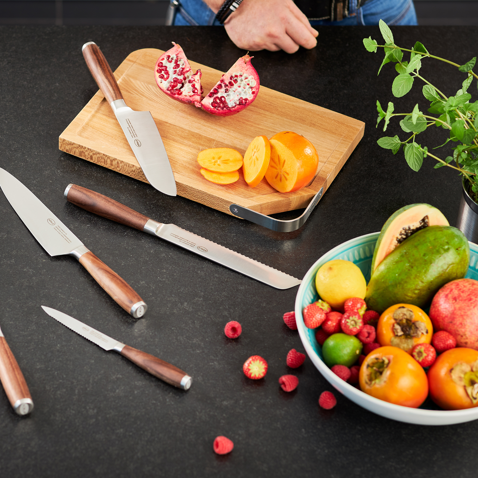 RÖSLE Schneidbrett mit Obst und Küchenmessern Schneidbrett aus Holz mit frischem Obst und Gemüse, darunter Granatapfel, Orange und Beeren,...