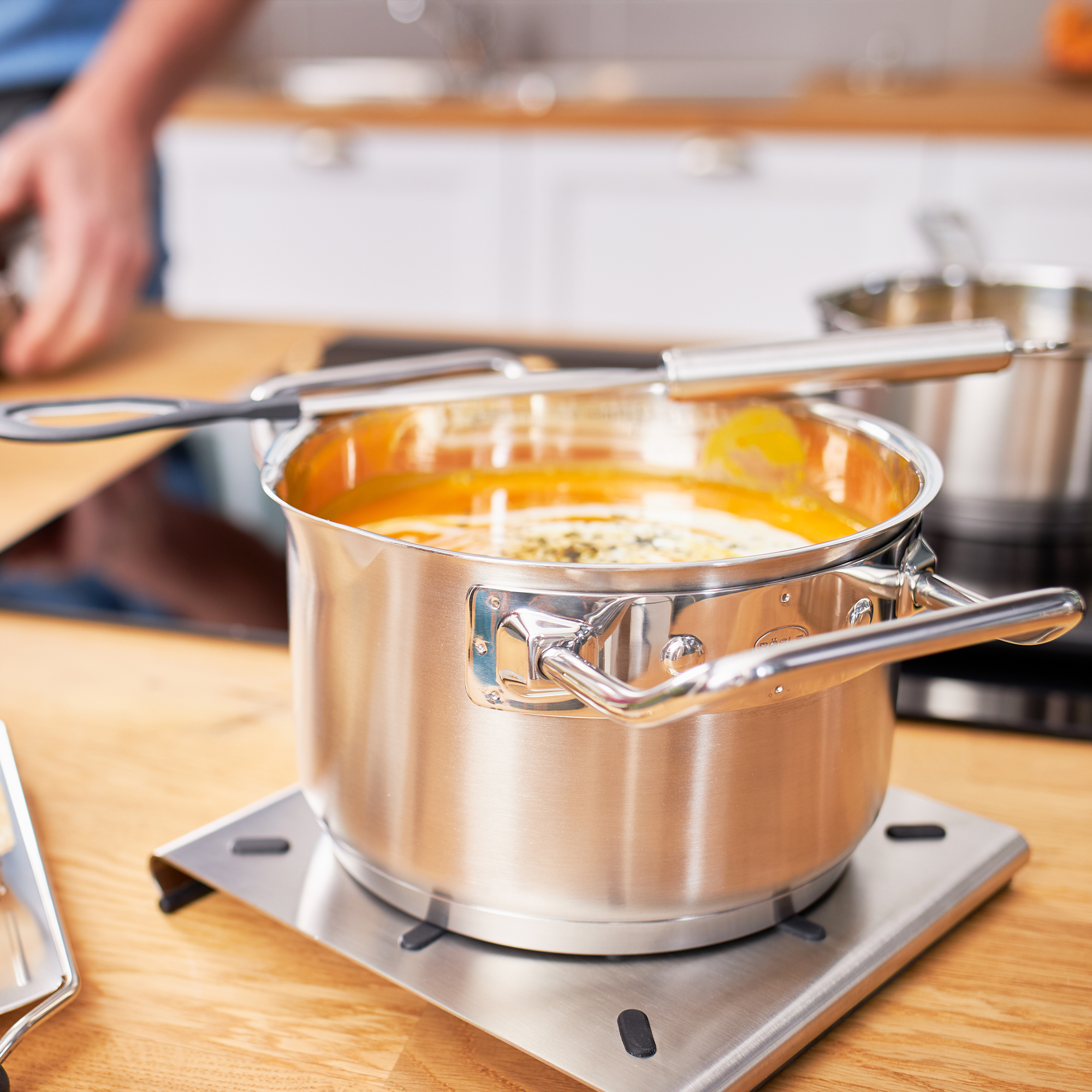 RÖSLE Kochtopf 16 cm auf Herd Kochtopf aus Edelstahl, 16 cm, mit Deckel und zwei Griffen, auf einem Herd mit orangefarbener...