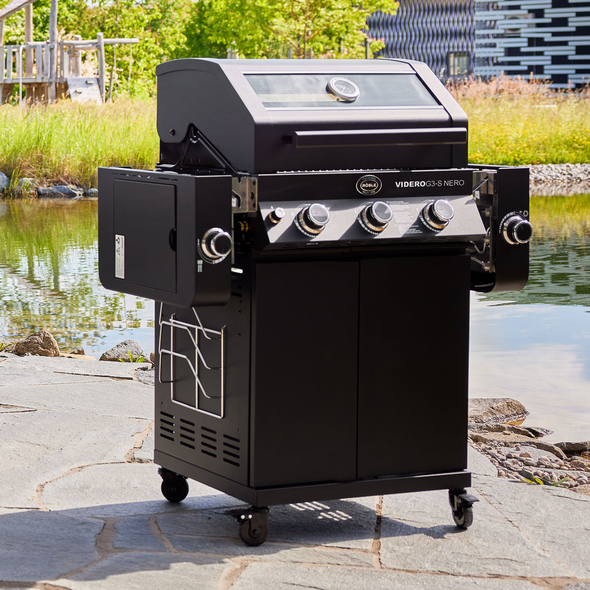 RÖSLE Gasgrill Videro G3-S NERO Gasgrill Videro G3-S in Schwarz mit vier Brennern und seitlichem Ablagetisch, auf einem Steinboden...