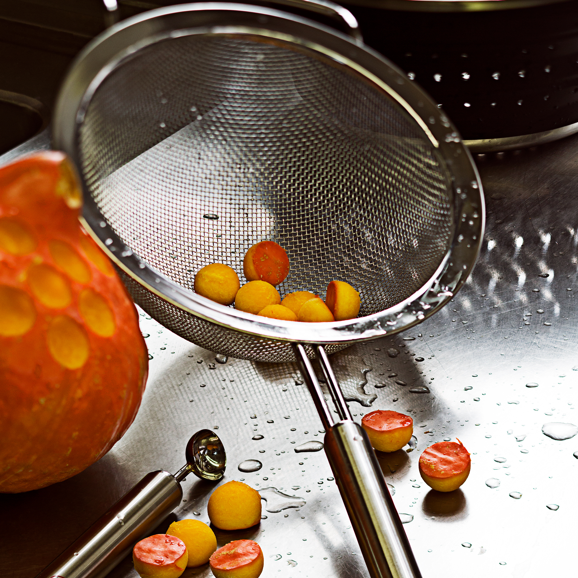 RÖSLE melon baller with melon balls Stainless steel ball cutter with orange-coloured melon balls on a wet work surface.