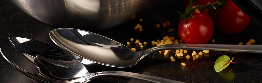 RÖSLE serving series stainless steel spoon Stainless steel serving series with shiny spoons, surrounded by tomatoes and a bowl.