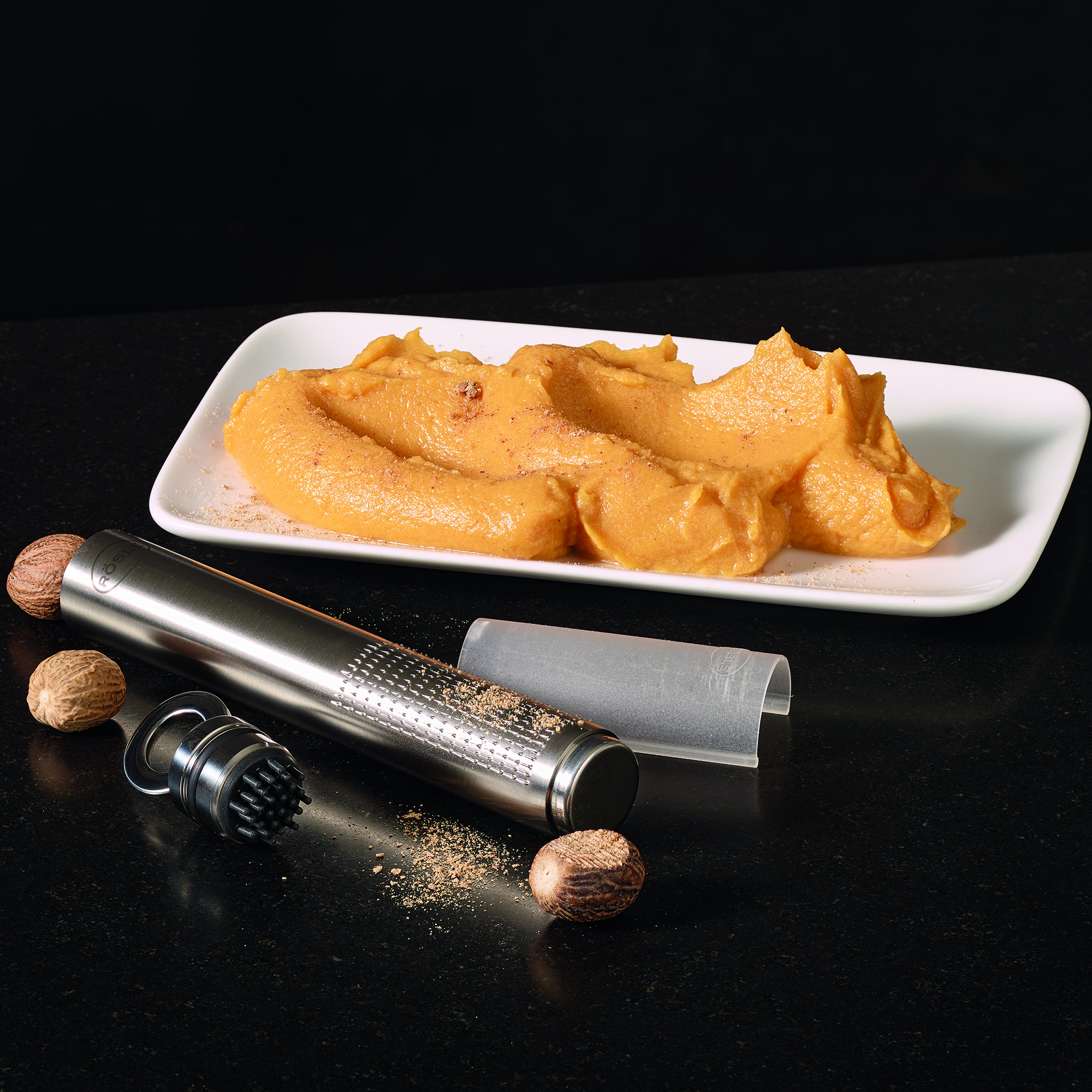 RÖSLE Muskatreibe und Muskatnüsse Muskatreibe aus Edelstahl, 18 cm, mit Muskatnüssen und geriebenem Muskat auf einem Teller.