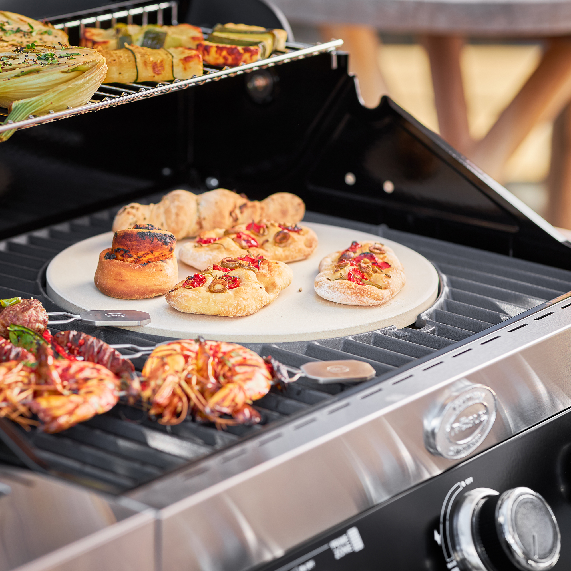 RÖSLE Pizzastein Vario auf dem Grill Pizzastein Vario auf einem Grill mit verschiedenen belegten Teigwaren und Meeresfrüchten.